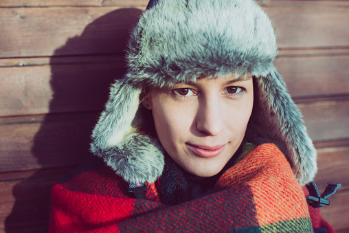 close up portrait of beautiful young woman, posing in warm hat and blanket over wooden background