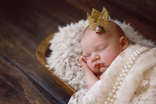 A newborn baby girl sleeps soundly. She is wearing a tiny golden crown. A princess is born! 