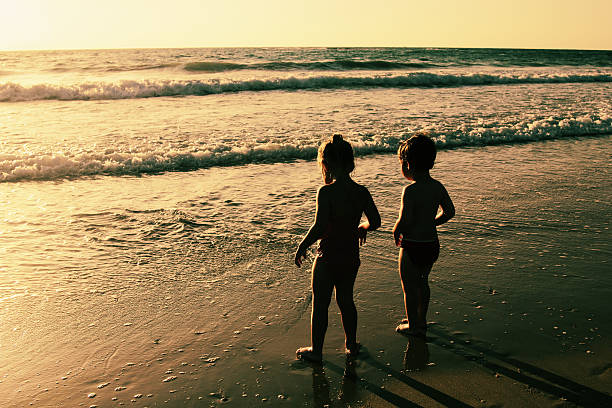 two happy kids playing on the beach at sunset