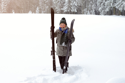 Fit active elderly lady with her skis standing in deep fresh snow in a rural winter landscape smiling at the camera, with copy space