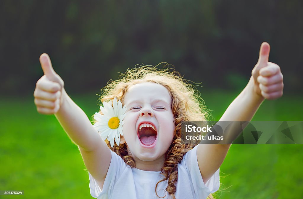 Laughing girl showing thumbs up. Laughing girl with daisy in her hairs, showing thumbs up. Child Stock Photo