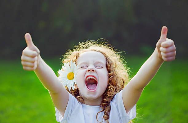 Laughing girl showing thumbs up. Laughing girl with daisy in her hairs, showing thumbs up. kids laughing stock pictures, royalty-free photos & images