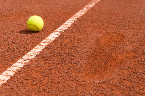 Tennis ball on clay with a footprint next to it