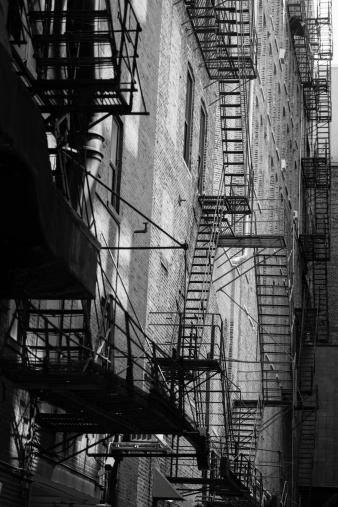 A monochrome image of the side of an old building with a fire escape.