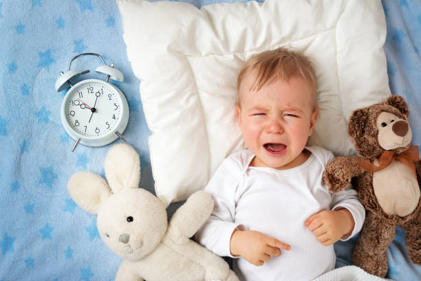 One year old baby with alarm clock One year old baby lying in bed with alarm clock and crying sick bunny stock pictures, royalty-free photos & images