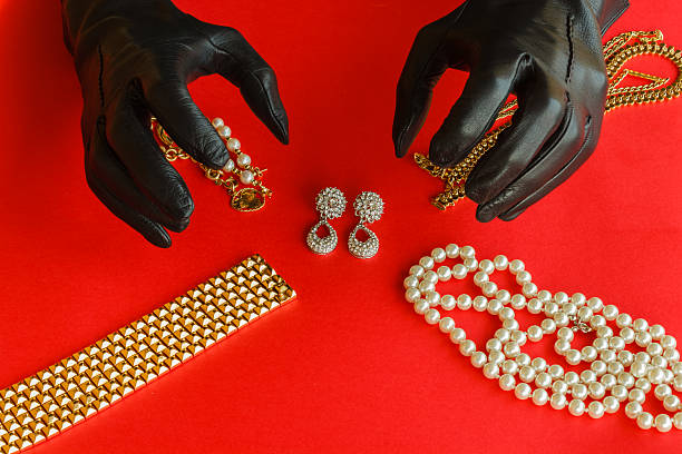 two hands  are going to steal the jewels two hands wrapped in black gloves are going to steal  a set  of necklaces,bracelets and  earrings of gold  and diamonds  placed on a red background wrap dress stock pictures, royalty-free photos & images