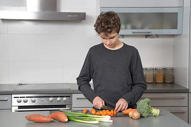 Teenage Boy in the kitchen cutting vegetables