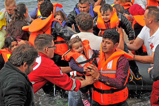 Lesvos, Greece- October 20, 2015: Refugees arriving in Greece in dingy boat from Turkey with Syrian, Afghanistan and African refugees . Volunteers help them to get out of the boat on the rocky beaches.