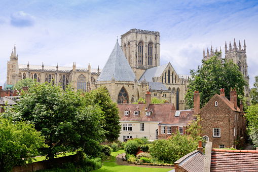 York Minster Cathedral, York, England, United Kingdom. York is a walled city in northeast England that was founded by the ancient Romans. Green trees, lawn, historic buildings and blue sky with clouds are in the image. HDR photorealistic image.
