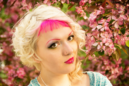Horizontal outdoor garden shot of young woman with blonde and pink hair in spring garden with flowering crab apple tree.
