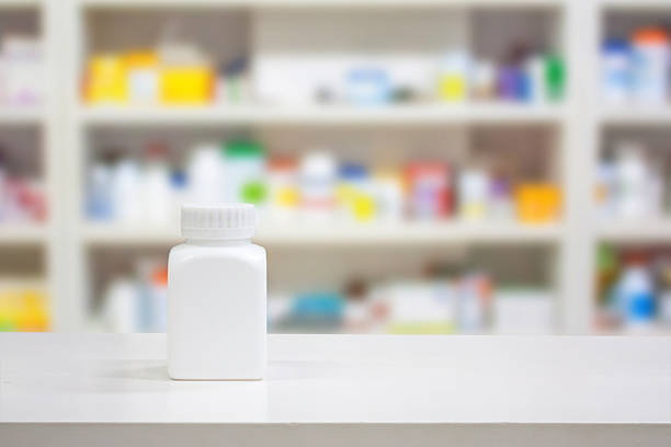 white medicine bottle on counter of drugstore Blank white medicine bottle on counter with blur shelves of drug in the pharmacy drugstore background over the counter meds stock pictures, royalty-free photos & images