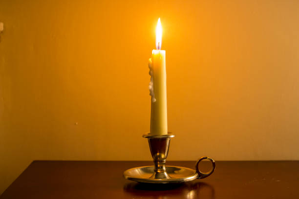 Vintage candle burning in antique candle holder on wooden table with plain background. 