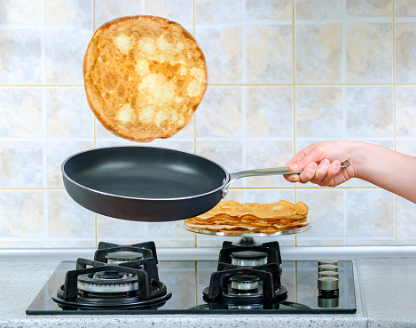 girl's hand holding a frying pan and turns the yeast pancake