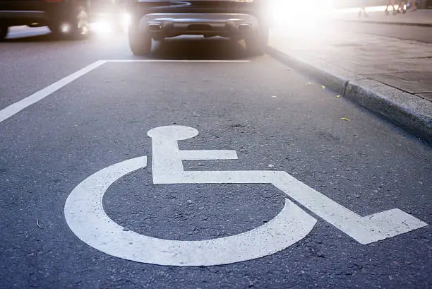 Photo of Handicap symbol on road, traffic and pedestrians in background