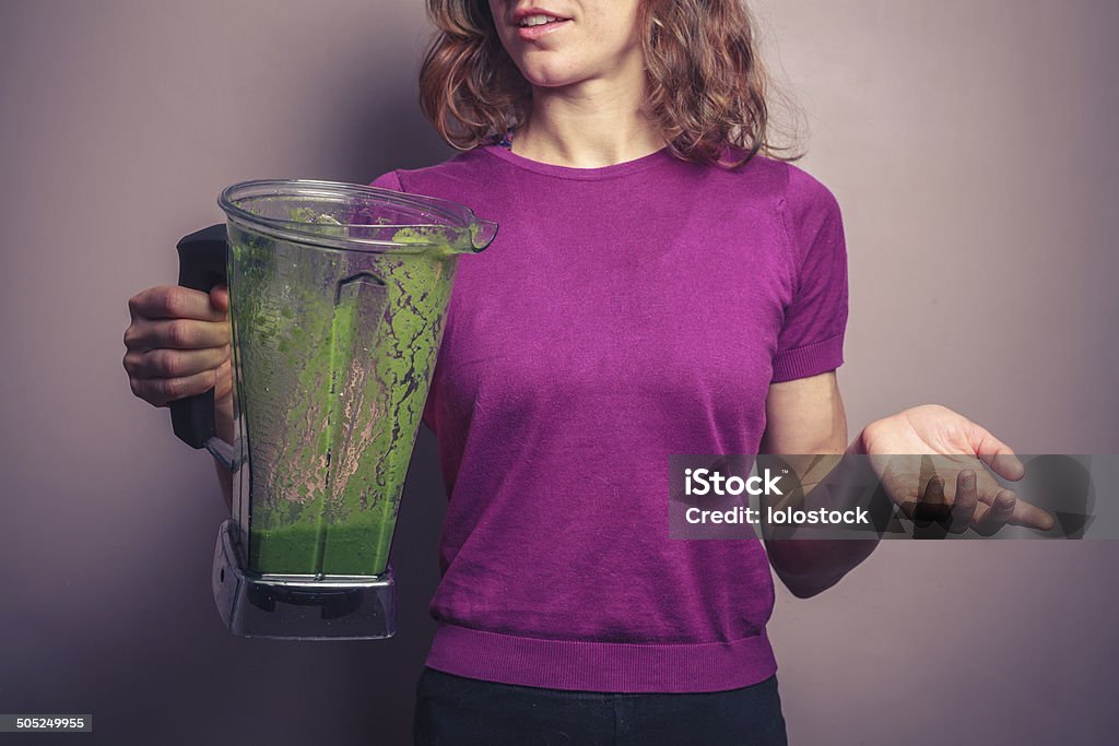 Young woman with green smoothie A young woman in a purple top is holding a blender with a green fruit smoothie Adult Stock Photo