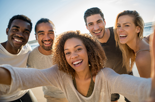 Group of Australian friends taking a selfie outdoors at the beach and looking at the camera smiling