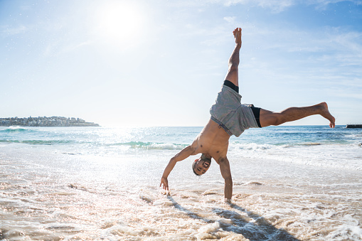 Handsome fit man doing a cartwheel at the beach and having fun outdoors