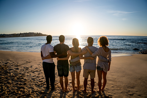 Group of friends at the beach enjoying the summer and looking at the beautiful sunset