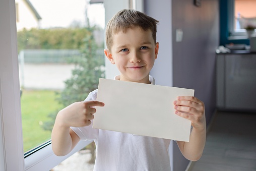 Happy boy in a polo shirt, holding an empty copyspace sheet of paper. Dressed in a white polo shirt