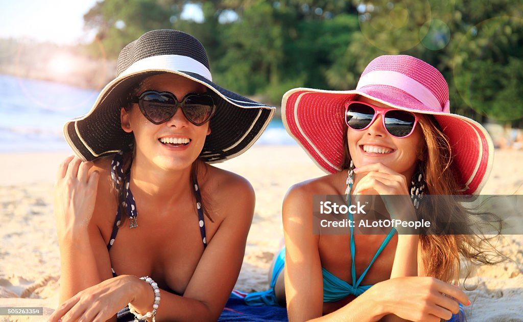 Women with sunhats Beautiful young women in sunhats laying on beach Beach Stock Photo