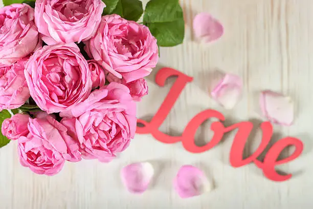 Pink roses and petals on wooden desk and red wooden word love