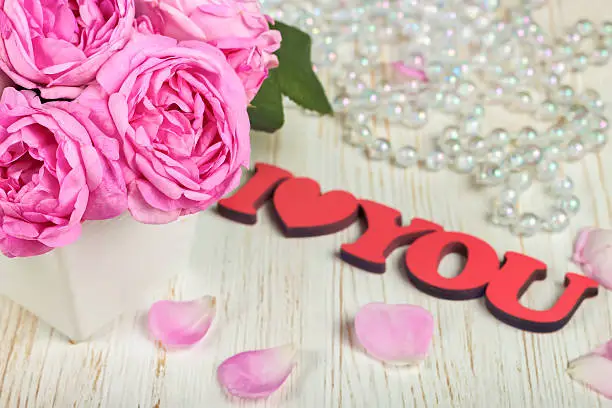 Pink roses and petals on white wooden desk and red wooden word