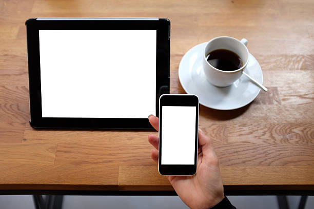 Woman hands holding smart phone with a cup of coffee and digital tablet in a coffee shop