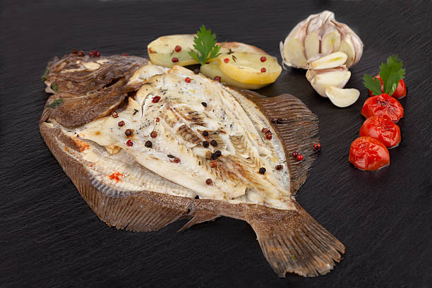 Plate Of Baked Turbot Fish Plate of baked turbot fish with potato slices, seasoned with garlic, cherry tomatoes, parsley, thyme, red and black pepper grains and black salt. turbot stock pictures, royalty-free photos & images