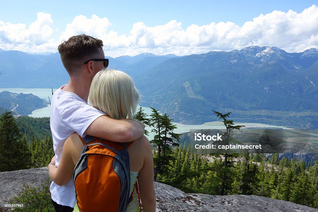 Loving couple admiring a magnificent view, shot from behind A couple stand on a high mountain ridge and gaze out at a stunning alpine view.  Couple - Relationship Stock Photo