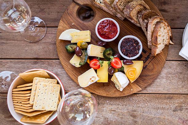 Delicious Platter Wine tasting with delicious cheese platter on a wooden board, with figs, olives, strawberry, homemade jams, plain crackers and tasty bread. plate fig blue cheese cheese stock pictures, royalty-free photos & images