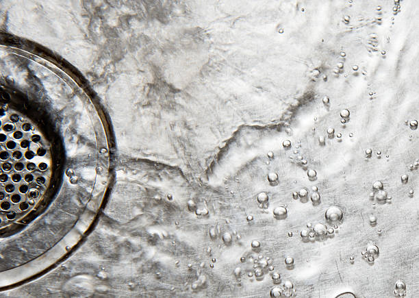 A close up photo taken of a Stainless steel sink drain strainer, of the water rushing down the drain with a wash and small bubbles with a grey silver colour look good for a background of some sort.
