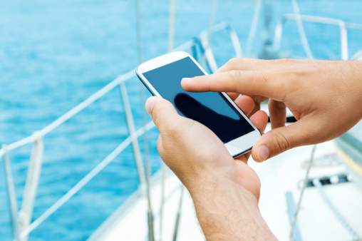 Male hands using smart phone on the sailboat, with sea in the background