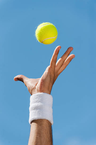 Serving tennis ball. Close-up of male hand in wristband throwing tennis ball against blue sky sweat band stock pictures, royalty-free photos & images