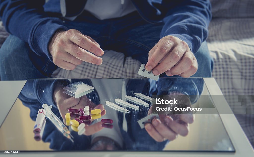 young drug addict man on hood sniffing cocaine on mirror young drugs addicted man on hood sniffing coke lines on mirror with rolled banknote and cutting razor blade at home alone Abuse Stock Photo