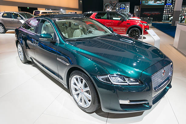 Brussels, Belgium - Januari 12, 2016: Green Jaguar XJ luxury saloon car front view. The car is on display during the 2016 Brussels Motor Show. The car is displayed on a motor show stand, with lights reflecting off of the body. There are people looking around and other cars on display in the background.