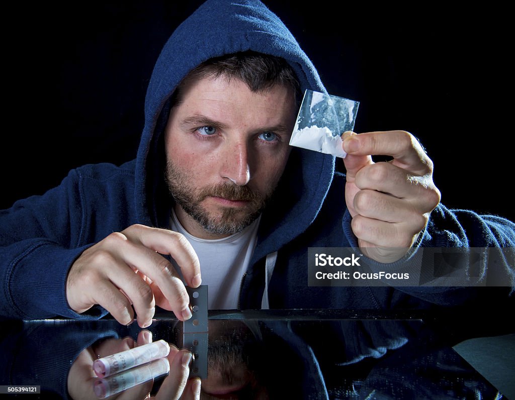 depressed sick looking Cocaine addict man sniffing coke depressed sick looking Cocaine addict man checking coke bag holding razor blade for cutting the drug and rolled banknote to snort the coke Abuse Stock Photo
