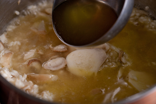 Ladle pour broth on pot of risotto with porcini mushrooms