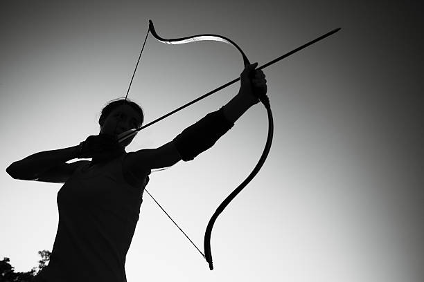 weibliche archer im feld bei sonnenuntergang - archery bow arrow women stock-fotos und bilder