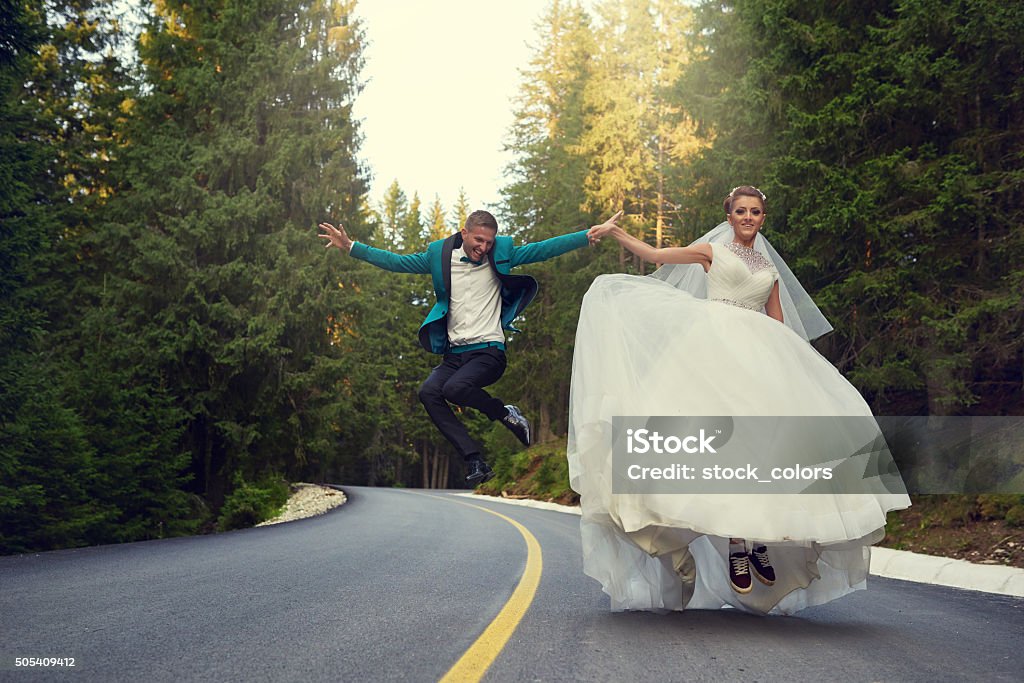 feeling the joy together bride and groom holding hands and jumping together, having fun on a street. Bride Stock Photo
