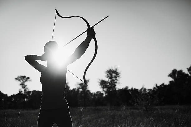 weibliche archer im feld bei sonnenuntergang - archery bow arrow women stock-fotos und bilder