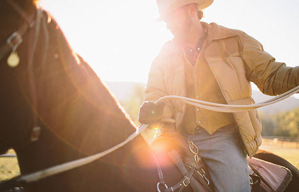 istock Sun glares as man holds back reins while riding horseback 505443277