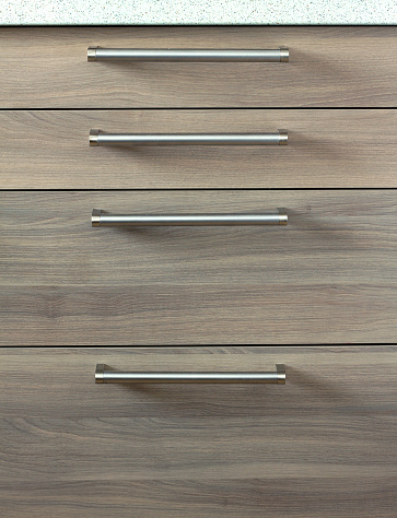 Front view of four closed sliding wooden drawers with metal long handles. Facade of modern kitchen furniture, vertical photo closeup
