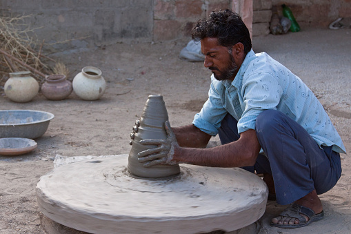 Rajasthan, India - March 10, 2015: Unidentified village potter creating a new vessel using traditional techniques. The stone wheel is started by using a stick to spin it and its speed is maintained in the same fashion