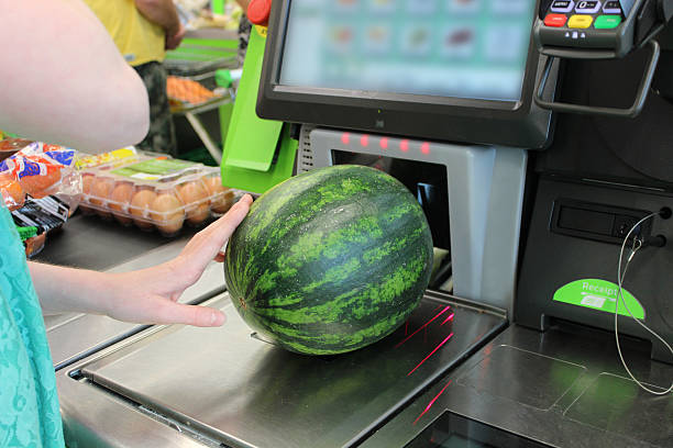 Girl scanning shopping (watermelon) at self-service supermarket checkout till (self-checkout) Photo showing a girl scanning her shopping (including a large green watermelon) at a self-service supermarket checkout till (also known as 'Self Checkouts' and 'Semi Attended Customer Activated Terminals' - SACAT. Self-service checkouts are quickly becoming commonplace in large supermarkets, reducing staff costs and replacing the need for cashiers. self checkout stock pictures, royalty-free photos & images