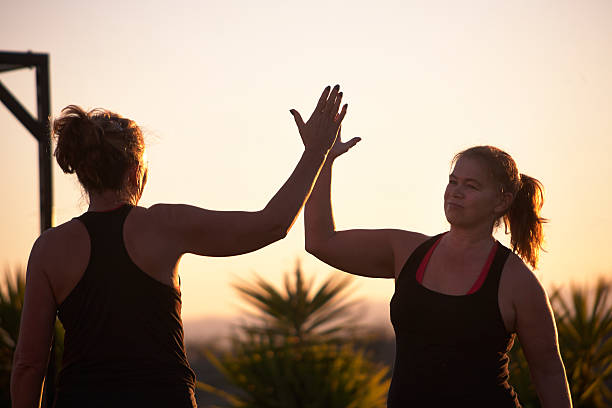 High Five! Two mature women doing a high five after an exercise class in the sunshine. military camp stock pictures, royalty-free photos & images