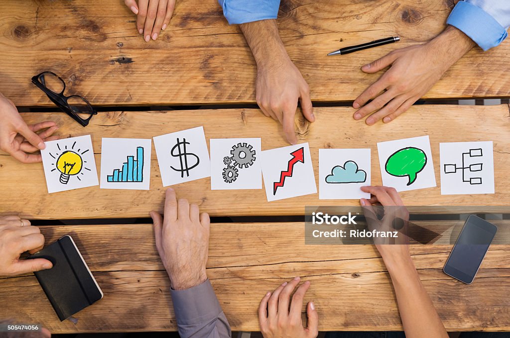 Business concepts on desk Businesspeople arranging different business concepts on wooden table. White cards strategy used by businesspeople. Business people brainstoring for new solutions while placing different cards in office. Small Business Stock Photo