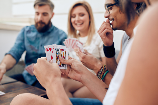 Group of friends sitting together playing cards. Focus on playing cards in hands of a woman during a party.