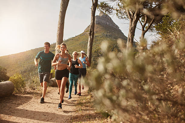 Group of fit people trail running on a mountain path Group of young adults training and running together through trails on the hillside outdoors in nature. Fit young people trail running on a mountain path. off track running stock pictures, royalty-free photos & images