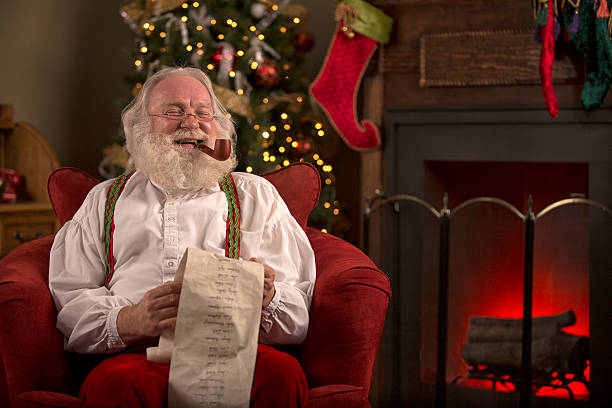 istock Santa Claus sitting at home, smoking a pipe, reading list 505482987