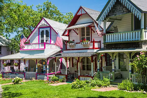 Three American flags fly in unison from the upper porches of brightly painted, ornate,  "gingerbread" style cottages in Oak Bluffs, Massachusetts on a late Spring afternoon.